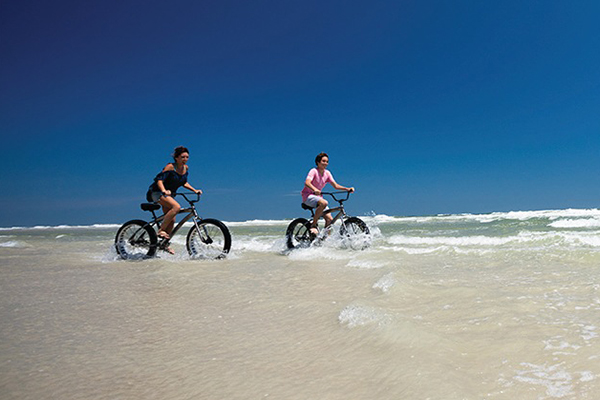 Two people riding bikes on beach